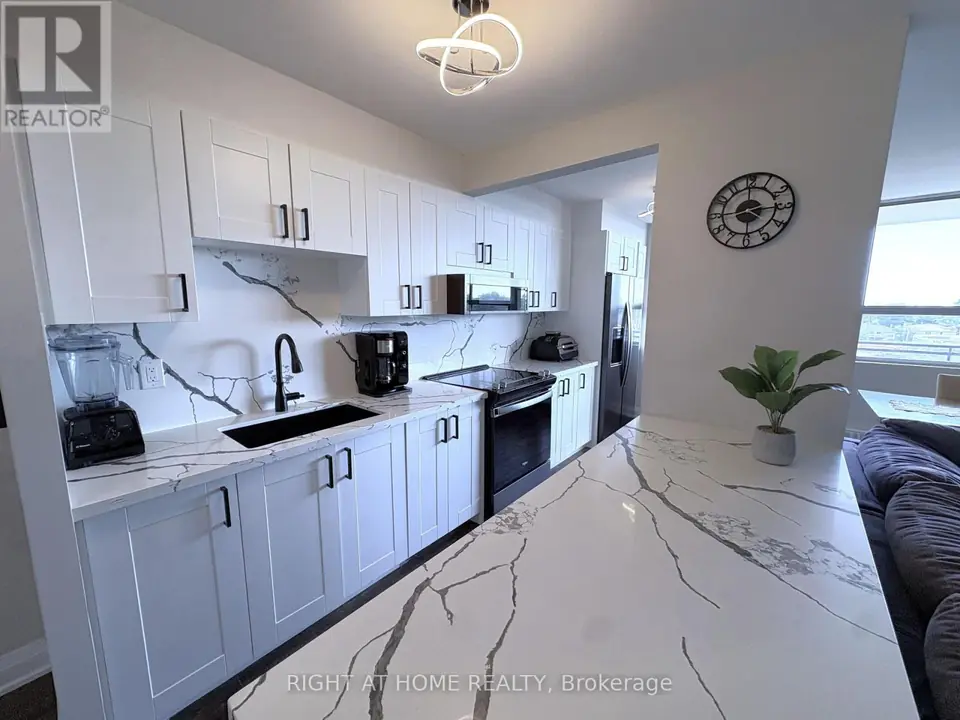 Galley kitchen with white cabinets, veined quartz backsplash, black sink and faucet, range, microwave and refrigerator beyond a quartz peninsula.